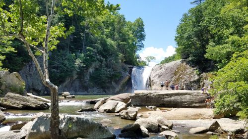 A scenic waterfall surrounded by lush greenery, with people exploring the rocky area and enjoying the natural beauty.