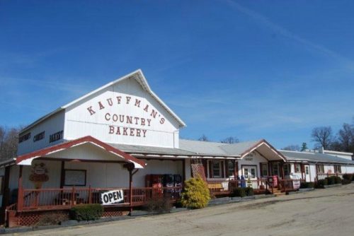 A rustic bakery building with a sign reading "Kauffman's Country Bakery," featuring a porch and an "Open" sign.