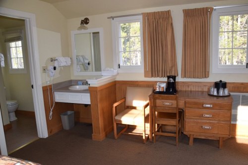Cozy hotel room featuring a bathroom, desk, chair, and coffee station with natural light from windows.