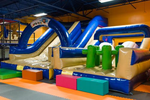 Colorful inflatable slides and obstacles in a play area, featuring blue, green, and pink elements on a padded floor.