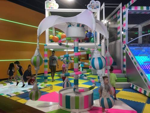 Colorful indoor play area with climbing structures, balls, and children playing on soft mats.
