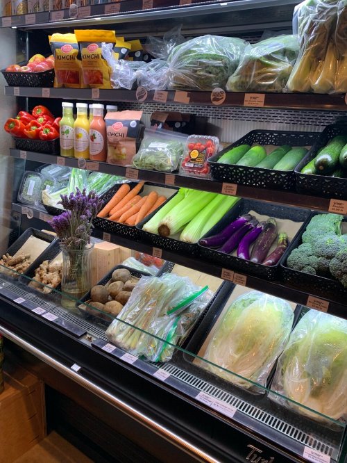 A display of fresh vegetables and fruits, including cucumbers, carrots, broccoli, and peppers, in a grocery store.