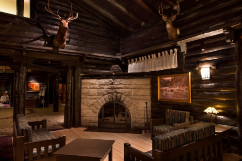Cozy log cabin interior featuring a stone fireplace, wooden furniture, and mounted deer heads on the walls.