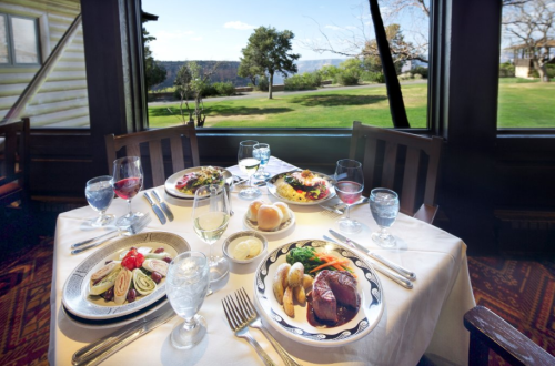 A beautifully set dining table with gourmet dishes and a scenic view of greenery outside.