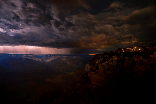 A dramatic night scene of the Grand Canyon with storm clouds and distant lightning illuminating the landscape.