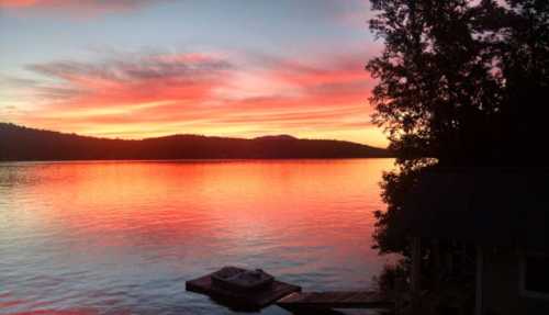 A vibrant sunset over a calm lake, with silhouettes of trees and mountains reflecting in the water.