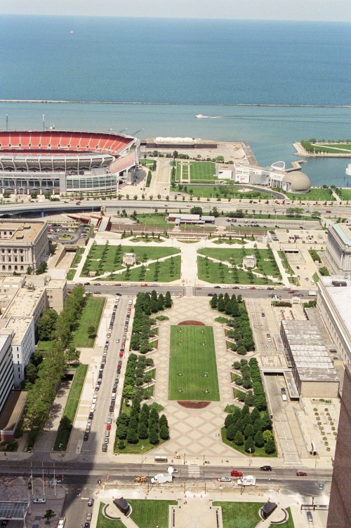Aerial view of a park with green spaces, pathways, and a stadium near a waterfront.
