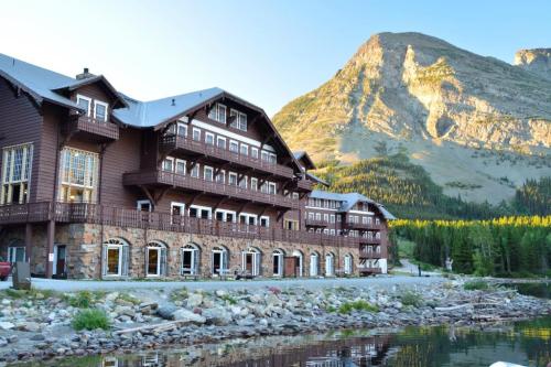 A rustic lodge by a serene lake, surrounded by mountains and lush greenery under a clear blue sky.