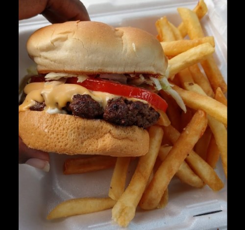 A close-up of a cheeseburger with lettuce and tomato, served with a side of golden French fries.