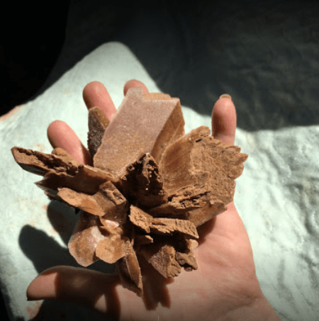 A hand holding a cluster of brown mineral crystals against a light background.