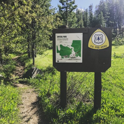 Sign for Crystal Park with a map, surrounded by greenery and trees, indicating a trail in a natural area.