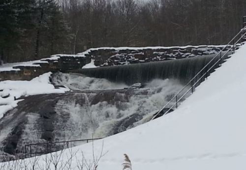 A snowy landscape featuring a waterfall cascading over rocks, surrounded by trees and a wintery scene.