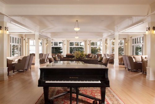 A spacious, elegant lounge featuring a grand piano, comfortable seating, and large windows with natural light.