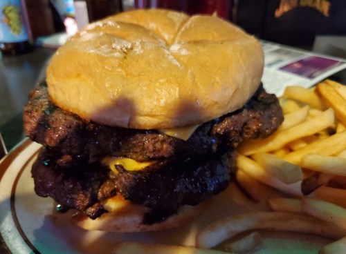 A stacked burger with melted cheese on a bun, served with a side of golden French fries.