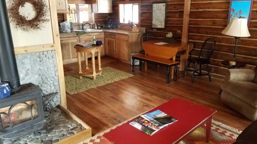 Cozy log cabin interior featuring a kitchen, dining area, and a wood stove with rustic decor and wooden furniture.