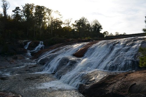 A serene waterfall cascading over rocky terrain, surrounded by trees and bathed in soft sunlight.