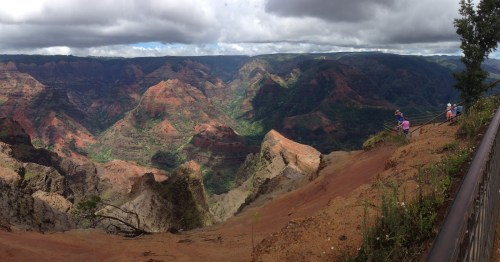 A panoramic view of a colorful canyon with lush greenery and dramatic rock formations under a cloudy sky.