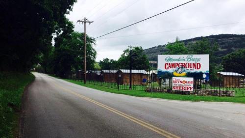 A scenic view of a road leading to Mountain Breeze Campground, with a large sign and trees in the background.
