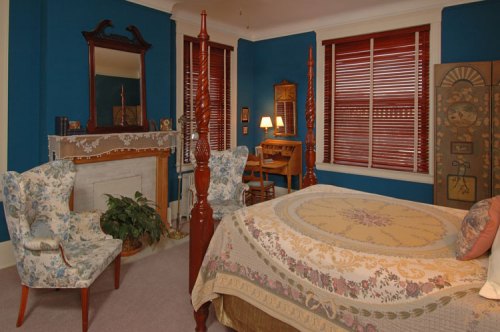 Cozy bedroom with blue walls, a patterned bedspread, vintage furniture, and a decorative fireplace.