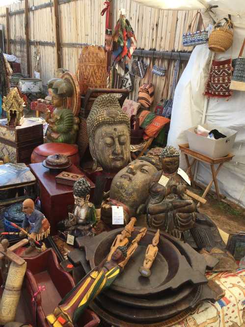 A vibrant market display featuring various wooden sculptures, Buddha figures, and handcrafted items in a tented space.