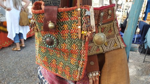 Colorful woven bags with intricate patterns and decorative embellishments displayed at a market.