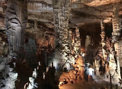 Stalactites and stalagmites in a dimly lit cave, showcasing intricate rock formations and natural beauty.