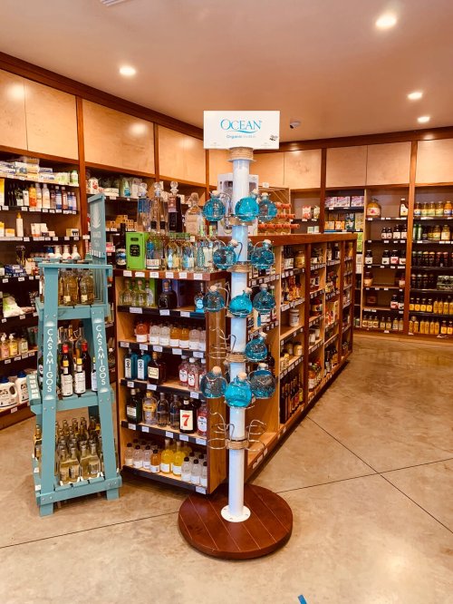 A display stand with blue glass bottles in a store aisle filled with various liquor bottles on shelves.