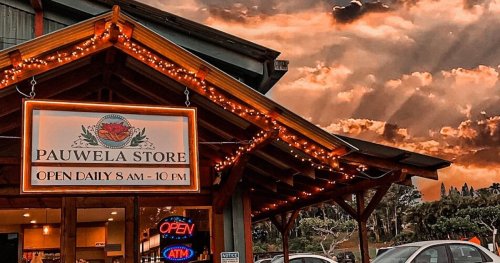 A charming store with a sign reading "Pauwela Store," illuminated by lights, set against a dramatic sky.