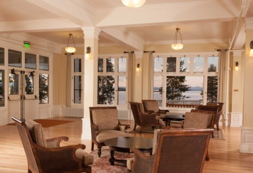 Cozy lounge area with armchairs and a round table, large windows showcasing a scenic view of trees and water.