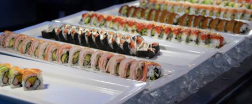 A variety of sushi rolls displayed on white platters over ice, featuring colorful ingredients and toppings.