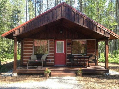 A cozy wooden cabin with a red roof, front porch, and surrounded by trees in a serene forest setting.