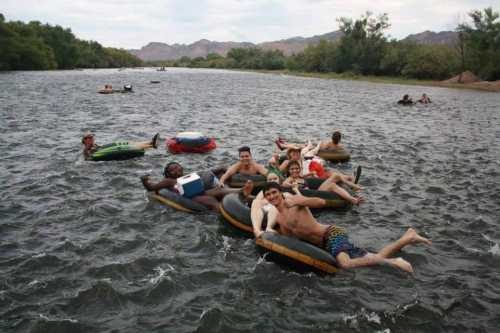 A group of people enjoying a fun day floating on inner tubes in a river, surrounded by trees and mountains.