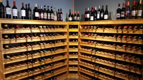 A wooden wine rack filled with various bottles of wine, displayed on shelves against a wall.