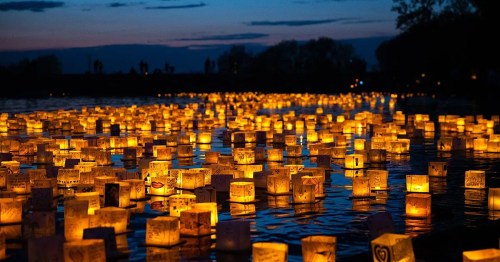A serene night scene of glowing lanterns floating on water, illuminating the dark with warm, golden light.