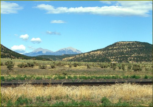 A scenic landscape featuring mountains in the background, rolling hills, and a grassy foreground with a railway track.