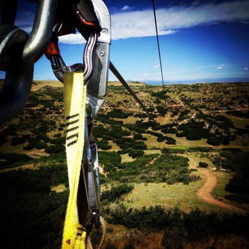 A close-up of a zip line harness and cable, overlooking a scenic landscape with hills and blue sky.