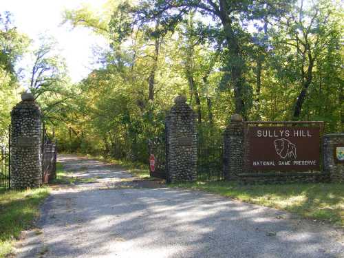 Entrance to Sully's Hill National Game Preserve, featuring stone pillars and a sign amidst lush greenery.