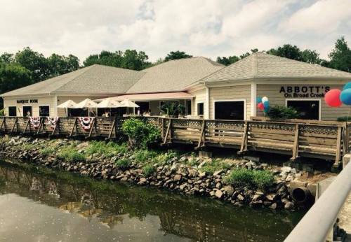 A waterfront restaurant with a wooden deck, decorated with balloons and bunting, surrounded by greenery and water.