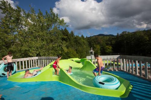 A water park scene with colorful slides, kids playing, and a scenic backdrop of trees and mountains under a cloudy sky.