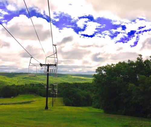 A scenic view of a ski lift with green hills and a cloudy blue sky in the background.