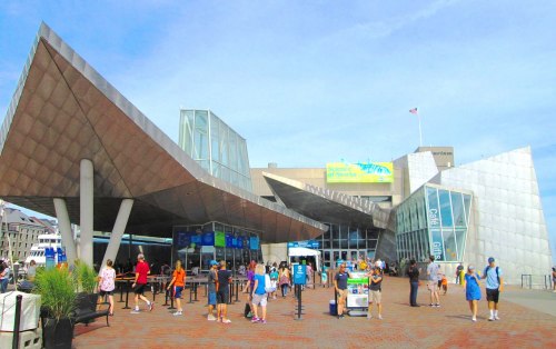 A modern building with a unique design, bustling with visitors outside on a sunny day.