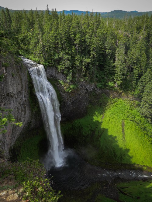 A stunning waterfall cascades down a rocky cliff, surrounded by lush green trees and a serene landscape.