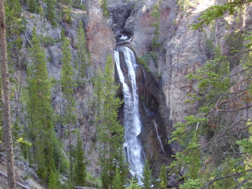 A waterfall cascading down rocky cliffs, surrounded by lush green trees in a natural landscape.