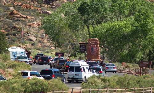 Traffic entering Zion National Park, with vehicles lined up near the park entrance surrounded by greenery and rocky terrain.