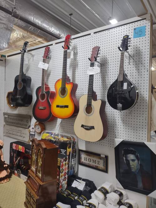 A display of various guitars and a mandolin hanging on a pegboard, with decorative items and a photo of Elvis nearby.