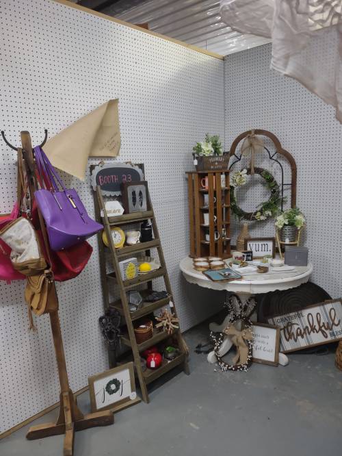 A cozy display featuring bags, decor, and a table with various items in a vintage-style booth.