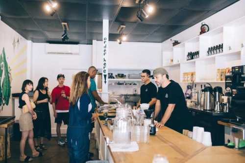 A busy coffee shop scene with customers ordering at the counter and baristas preparing drinks.