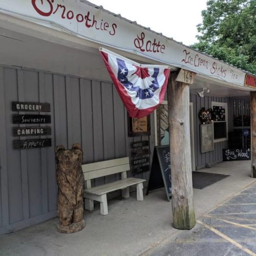 A small shop with a sign for smoothies and ice cream, featuring a patriotic banner and outdoor seating.