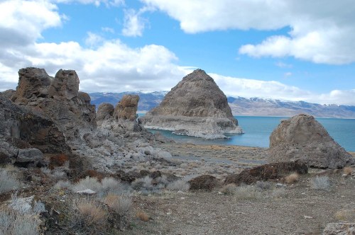 A rocky landscape with unique formations and a large island in a blue lake under a cloudy sky.
