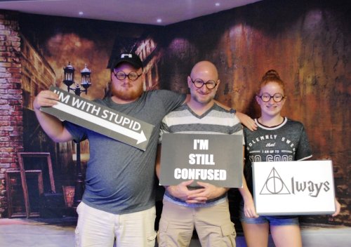 Three people pose with humorous signs: one says "I'm with stupid," another "I'm still confused," and the last "Always."